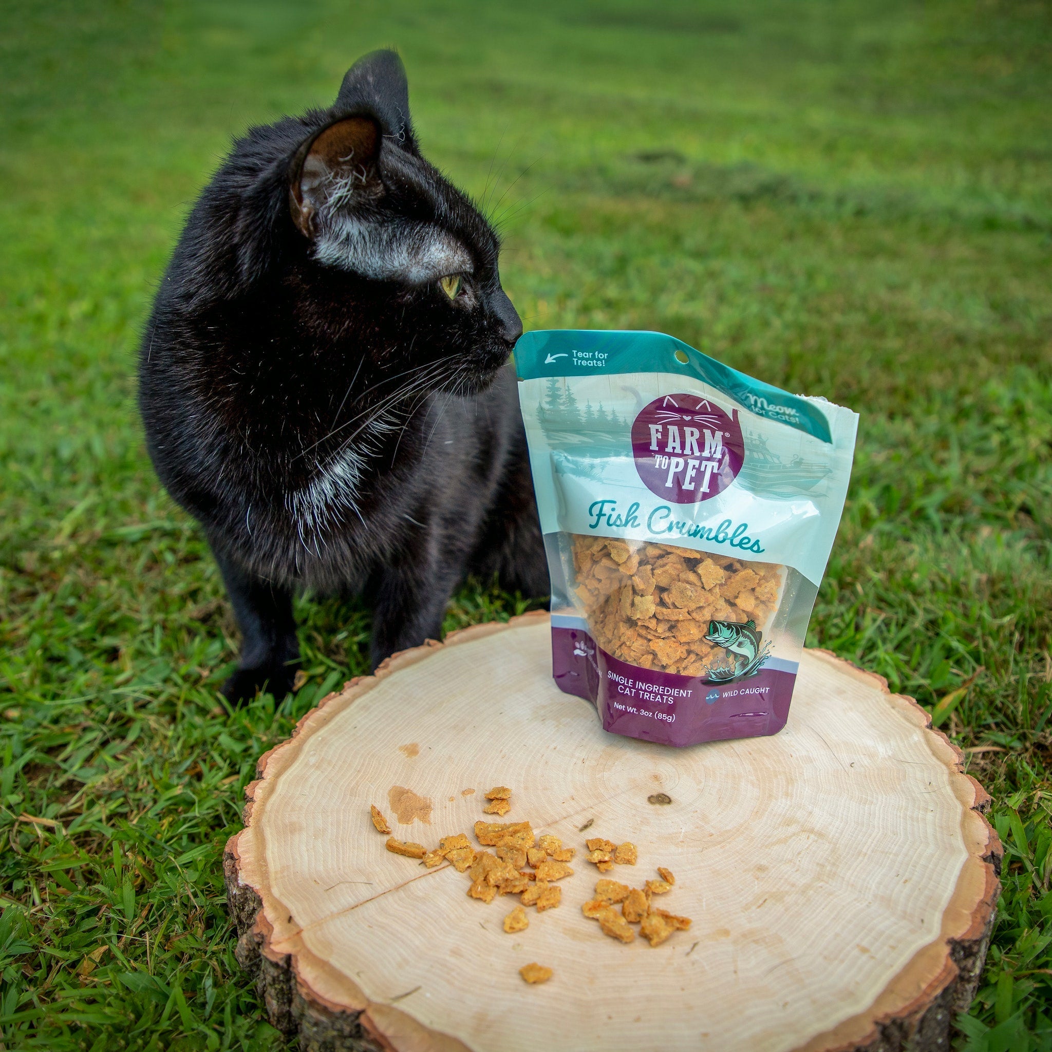 Cat treats fish crumbles pouch with scattered brown crumbles on a cut log
