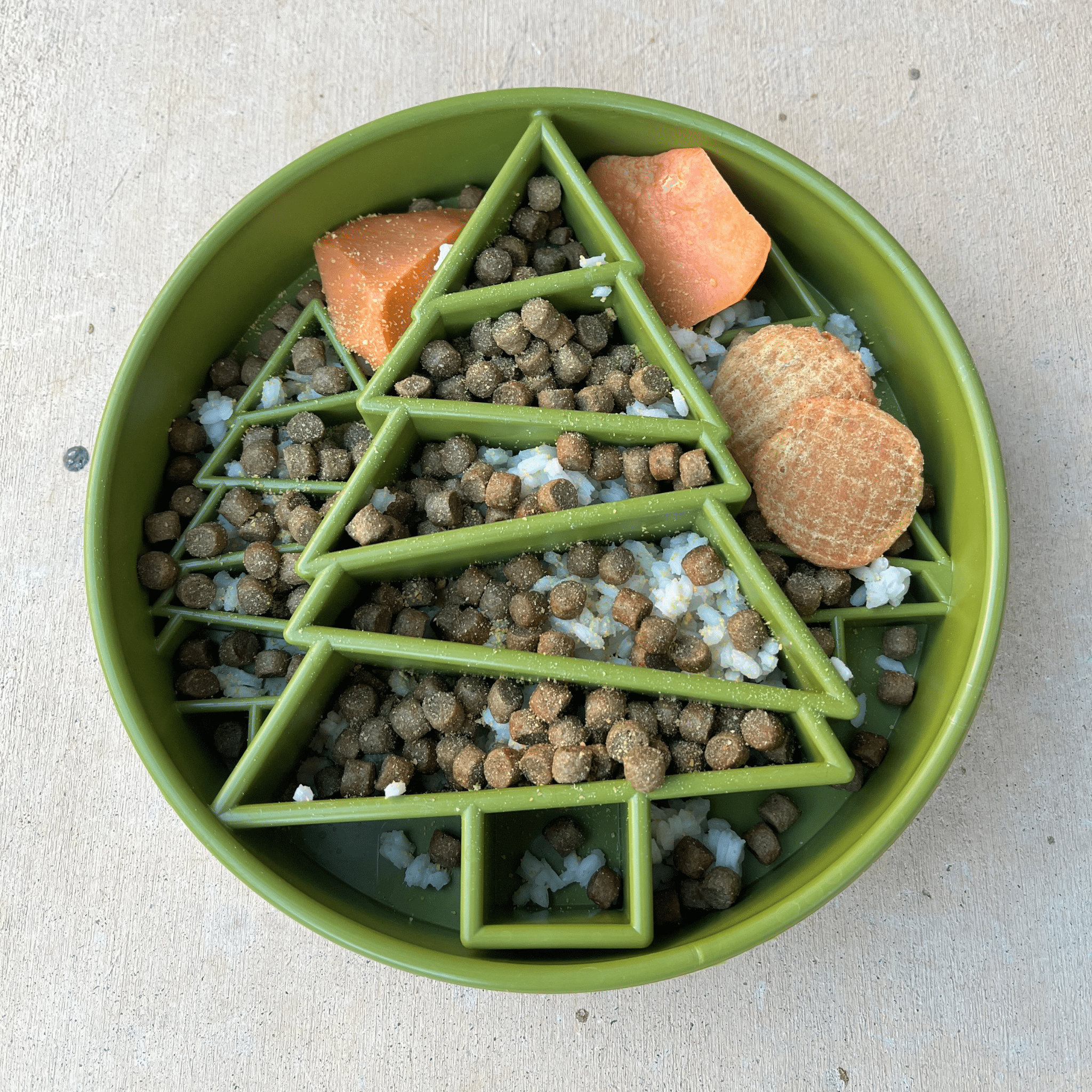 Green slow feeder dog bowl filled with kibble and treat pieces in tree maze
