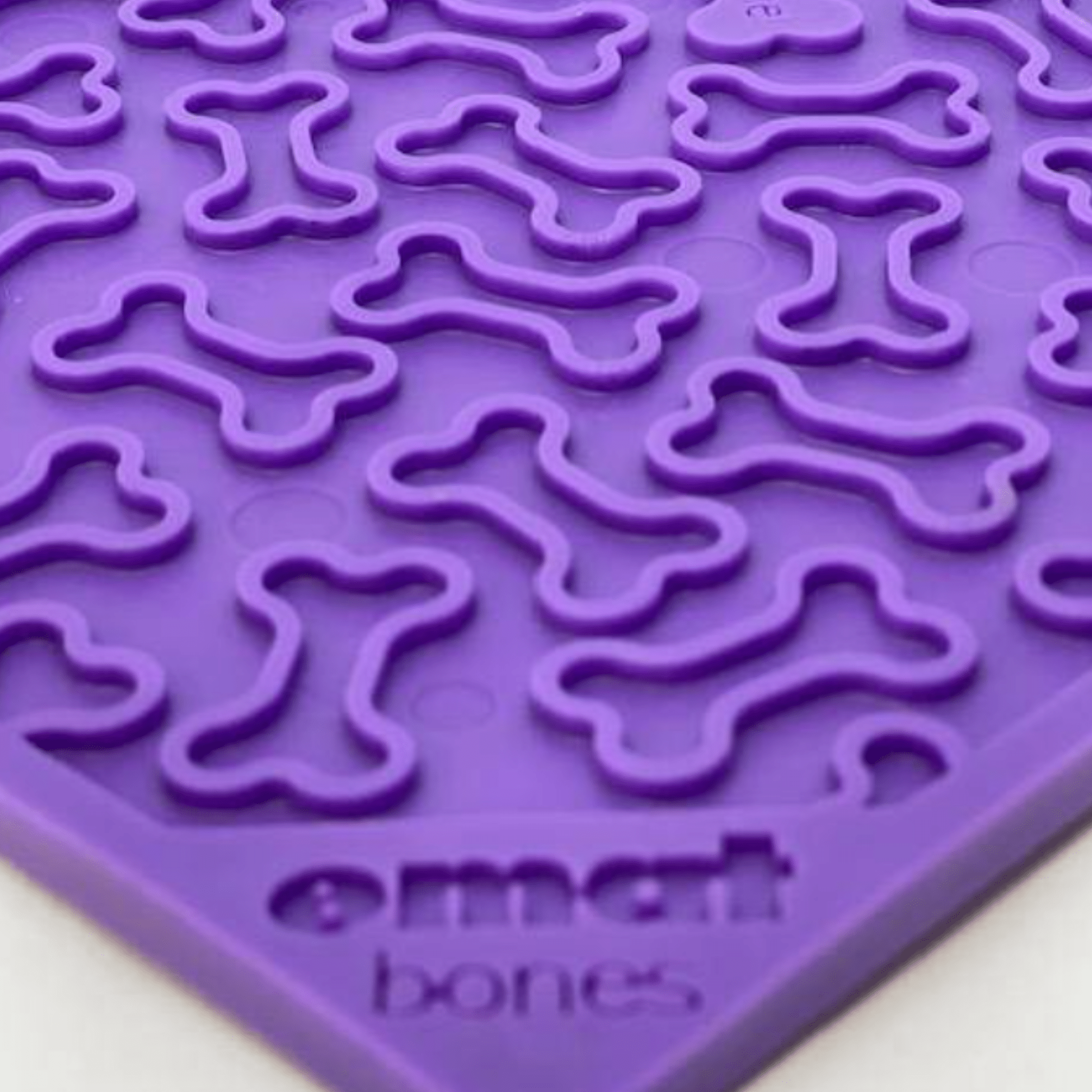 Purple dog lick mat close-up with raised bone grooves on textured silicone surface.