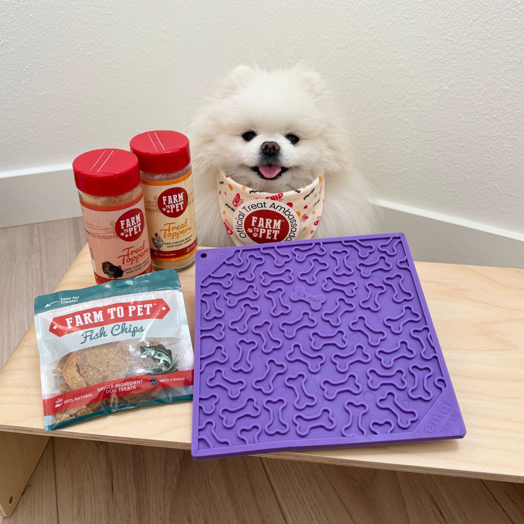 Purple dog lick mat on a wooden table with dog licking and treat containers.