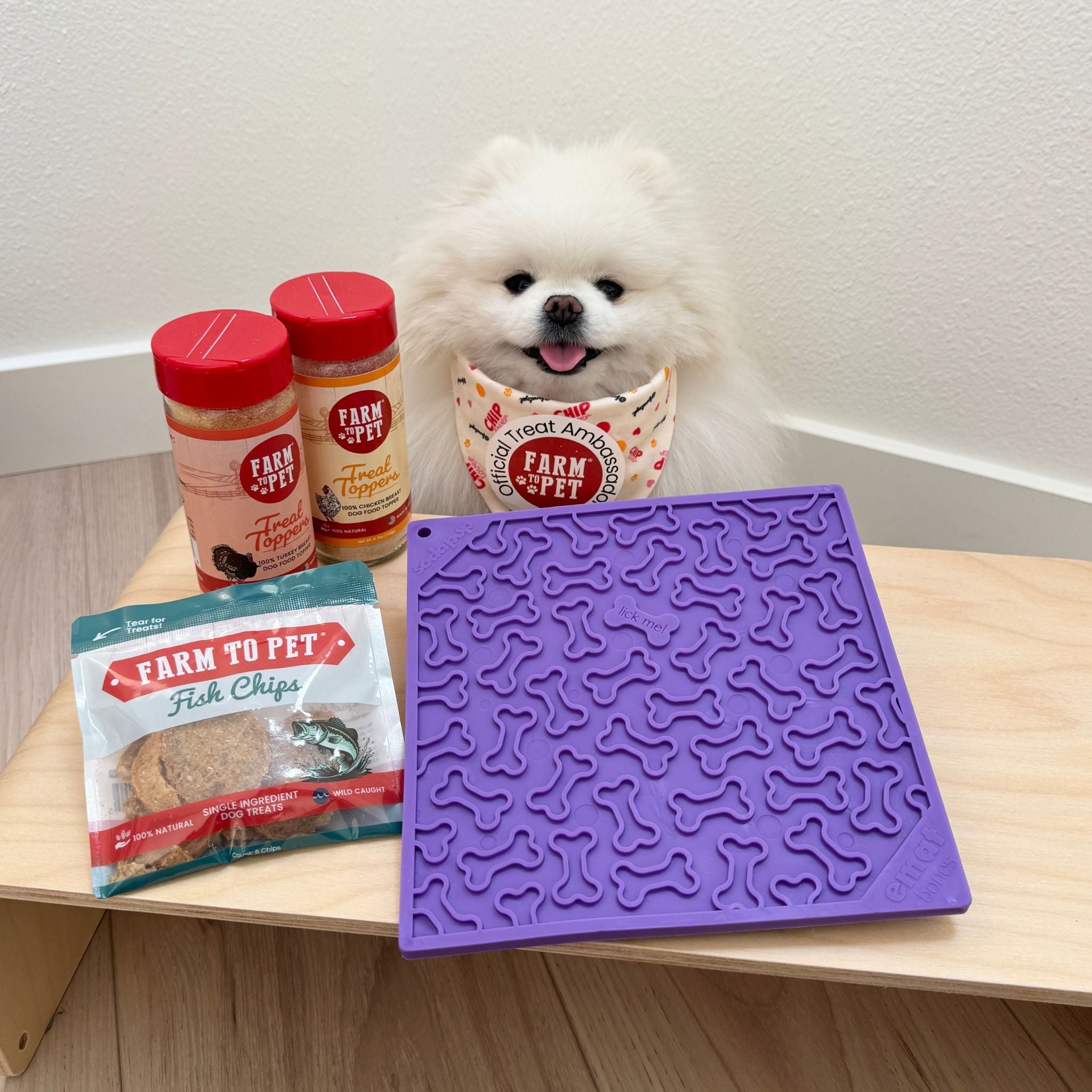 Purple dog lick mat on a wooden table with dog licking and treat containers.