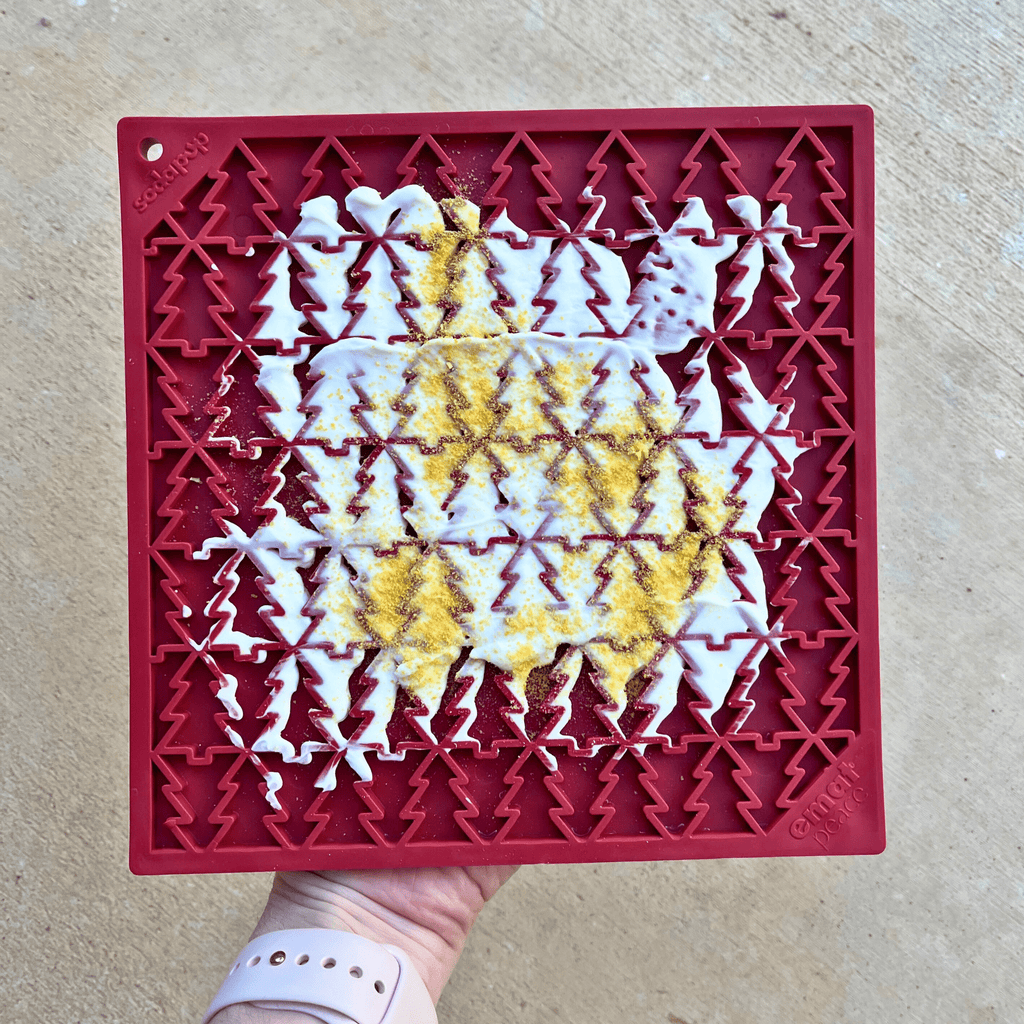 Red silicone lick mat with raised tree pattern holding smeared treats