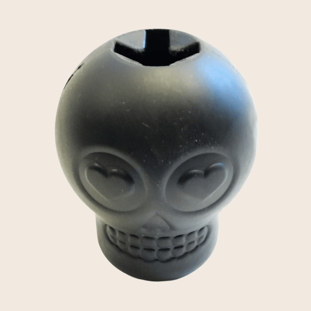 Skull-shaped dog treat dispenser, dark gray with opening on top and heart eyes.