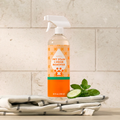 Orange-and-clear pet odor remover spray bottle with cucumber-mint scent, on folded towels